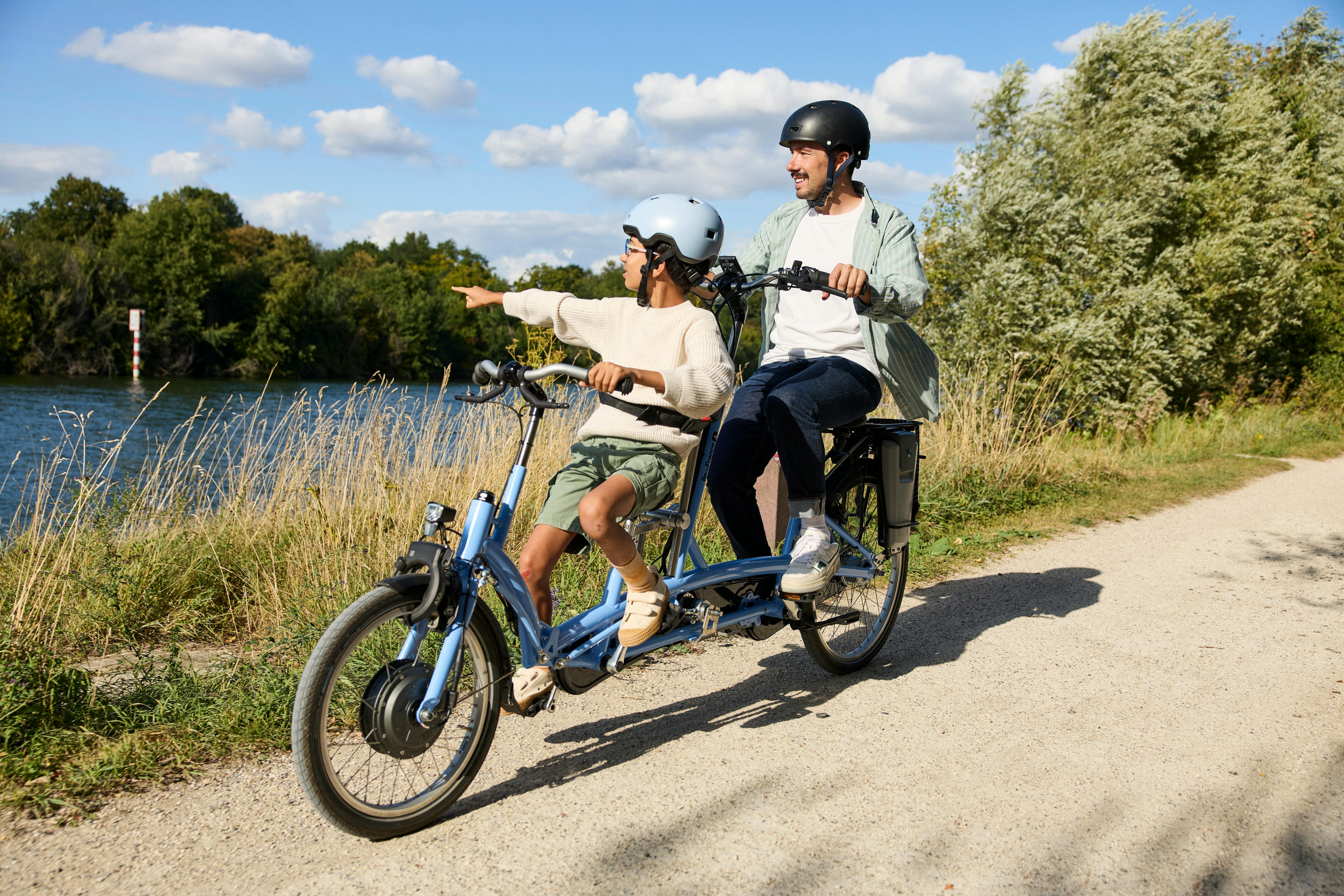 Un adulte et un enfant sont sur un vélo tandem adulte-enfant Véligo sur une voie verte au bord d'une rivière