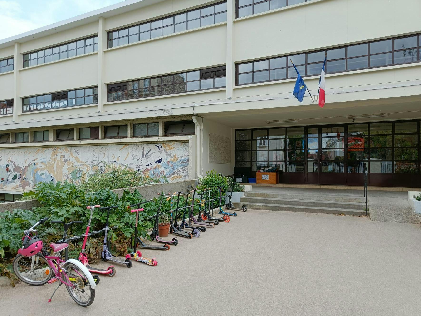Vélo et trottinettes de taille enfant stationnés sur des emplacements dédiés devant une école primaire